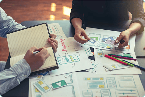 Hands sketching product diagrams on a cluttered desk